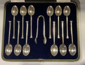 A set of twelve George V silver teaspoons, monogrammed stepped terminals, a pair of sugar bows en