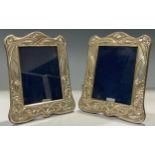 A pair of Elizabeth II silver Art Nouveau style arched easel photograph frames, embossed with