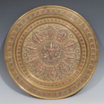 An Indian brass and copper circular charger, chased and applied with deities , leaves and