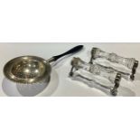 A pair of George V silver mounted knife rests, Chester 1930; a silver tea strainer, Birmingham