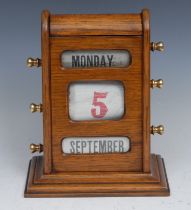 An early 20th century oak perpetual desk calendar, domed cresting above glazed apertures for day,