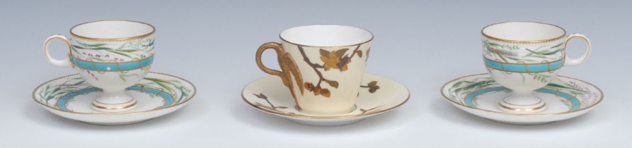 A pair of Royal Worcester pedestal teacups and saucers, painted with grasses over a raised gilt