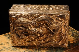 A Japanese silver rectangular box and cover, chased in bold relief with a dragon above crashing