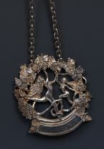 An Elizabeth II silver wine label, cast with nude maenads dancing beneath fruiting vine, 5cm wide,