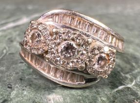A diamond cluster ring, twisting crown set with three round brilliant and thirty four baguatte cut
