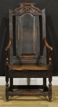 A 17th century oak armchair, the tall back with shaped and carved cresting above a raised and