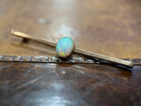 An opal and gold coloured metal bar brooch, the single oval cabochon stone centered on a plain