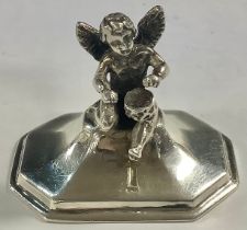 A silver menu holder, as a cherub beating drum