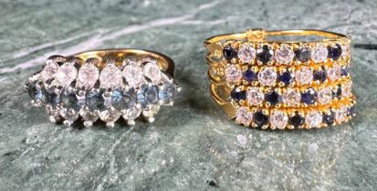 A gold coloured metal cluster dress ring, set with a row of blue coloured stones flanked by two