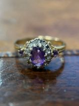 A 9ct gold, amethyst and diamond cluster ring, the central oval facet cut stone within a band of