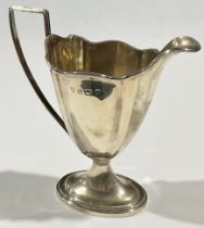 An Edwardian silver pedestal helmet shaped cream jug, angular reeded handle, stepped oval base,