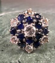 An 18ct gold diamond and sapphire flowerhead cluster ring, the central brilliant cut diamond flanked