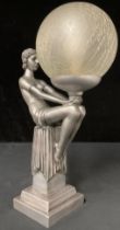 An Art Deco style table lamp, moulded as a semi-clad female nude, seated with globe, crackle glass