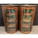 A pair of Edwardian mahogany bow front corner cabinets, wall mountable, of narrow proportions,