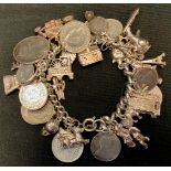A silver charm bracelet, suspending over thirty charms and coins, 132g gross