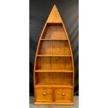 A stained pine boat-shaped open bookcase, three tiers of shelving above a pair of deep drawers, (