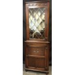 A Jaycee oak floor-standing corner cabinet, moulded cornice, carved frieze, leaded glass to top