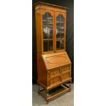 An oak narrow bookcase bureau, out-swept cornice, pair of astral-glazed doors enclosing three