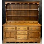 A George III style country kitchen oak dresser, shaped cornice, three tier plate rack top with seven