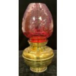 A large brass Veritas oil lamp, cranberry glass shade, 48cm high