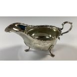 A George V silver sauce boat, scroll border, loop handle, three acanthus capped slender cabriole
