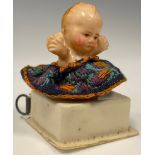A novelty sewing tape measure, as a baby kneeling, floral skirt, 4.6cm high.