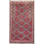A Persian hand knotted prayer rug, the filed with three lines of geometric lozenges, in tones of