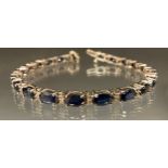 A diamond and blue sapphire tennis bracelet, white metal mounts, stamped 14k, 17cm long, 13.3g gross