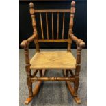 An early 20th century elm spindle-back rocking chair, turned arms and stretchers, woven rush seat,