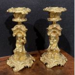 A pair of French Rococo style gilt bronze candlesticks, each stem with seated putti within sculpture