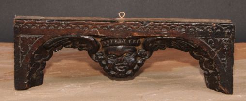 An early English oak carving, centred by a mask with arched and plumed wings, lunette border, 28cm