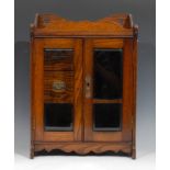 A late Victorian oak smoking room cabinert, shaped cresting above a pair of bevelled glazed doors
