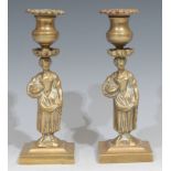 A pair of Regency bronze figural candlesticks, each cast as a young lady gathering flowers,