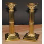 A pair of brass Corinthian column candlesticks, detachable nozzles, fluted columns, stepped square