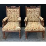 A pair of Edwardian carved oak library chairs, carved cresting rail and arms, button back and