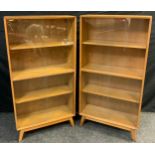 A pair of mid century oak bookcase cabinets, each with three tiers of shelving, enclosed within pair