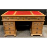 A oak pedestal desk, faux red leather inset writing surface, over-sailing top, pair of long frieze