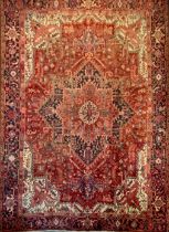 A Persian Heriz carpet, central geometric floral medallion within red ground, surrounded by triple