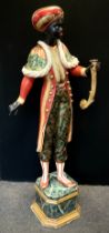A Venetian style carved and painted Blackamoor figure, standing on marble effect plinth, holding a