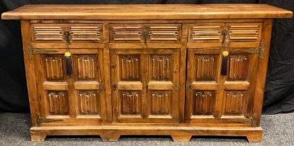 A contemporary walnut sideboard, three short drawers to frieze, above three cupboard doors, carved