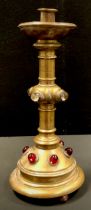 An Arts and Crafts brass altar candlestick, inset with ruby coloured and clear glass cabochons, on