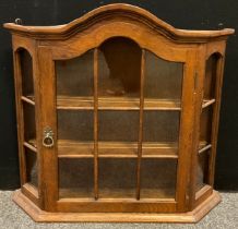 An oak wall-mounted cabinet, serpentine shaped top, canted front, glazed door, and sides, 66cm