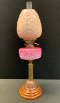 A Victorian oil lamp, pink milk glass reservoir, copper column, floral shade, wooden foot, 67cm high