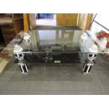 A glass coffee table with chrome black and white ornate legs