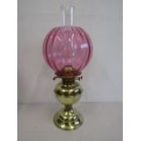 A brass base oil lamp with cranberry glass globe with spare funnel and wicks, in working order and