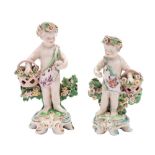 Two Chelsea-Derby figures of putti each holding a basket of flowers and on rococo scrollwork mound