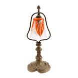 A brass table/student's lamp with foliate and scroll decorated base, orange and clear glass shade,