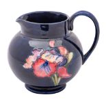 A Moorcroft pottery jug, tube lined in the Orchid pattern in red, yellow and green on a blue ground,