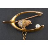 A brooch designed as a tri-colour chick within a wishbone beside a cultured pearl egg,