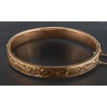 An early 20th century 9ct gold, hinged bangle, with engraved foliate and floral decoration,